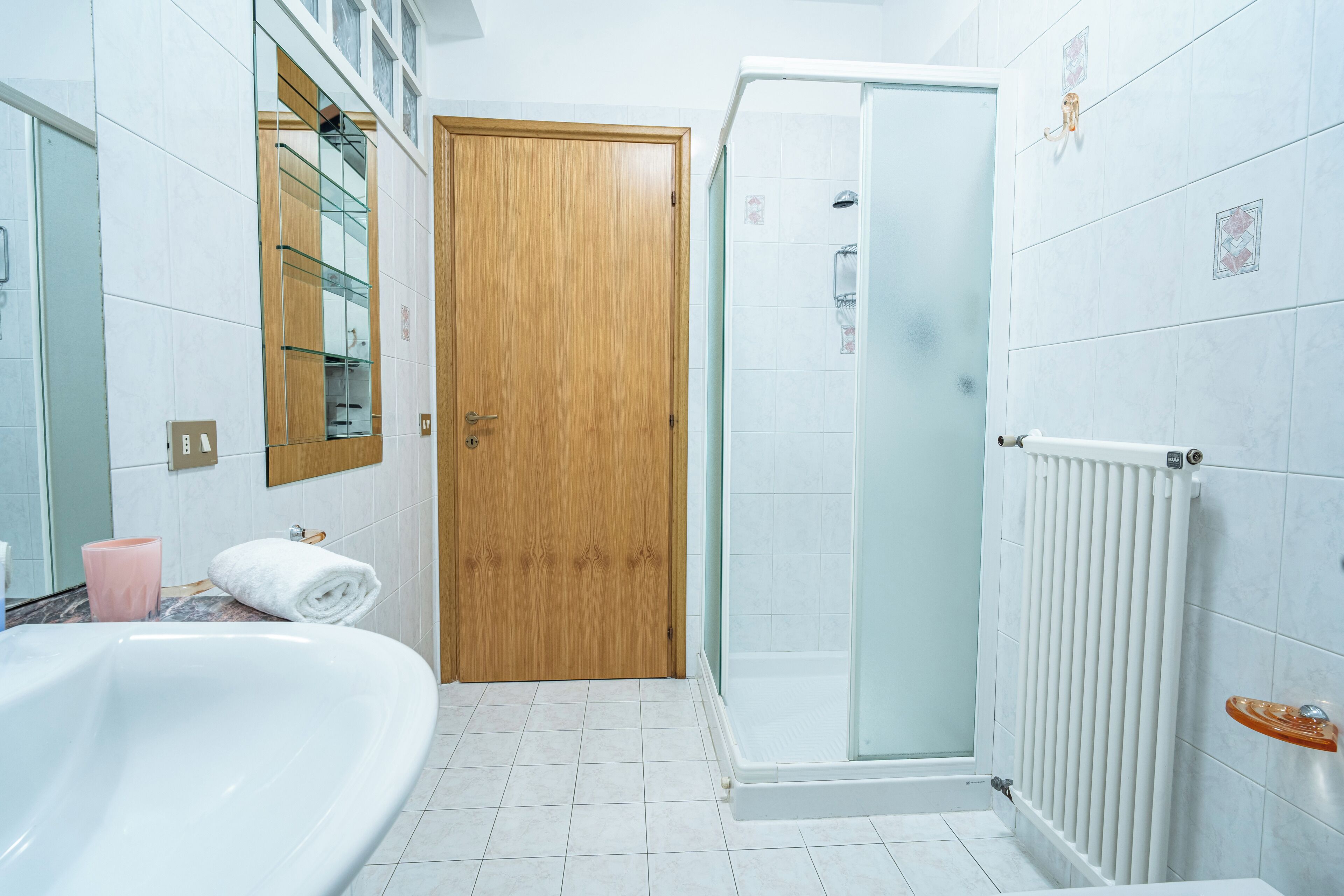 A bathroom with a bathtub, a glass shower enclosure, a wooden door, and a white radiator.