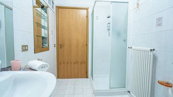 Une salle de bain avec une baignoire, une cabine de douche en verre, une porte en bois et un radiateur blanc.
