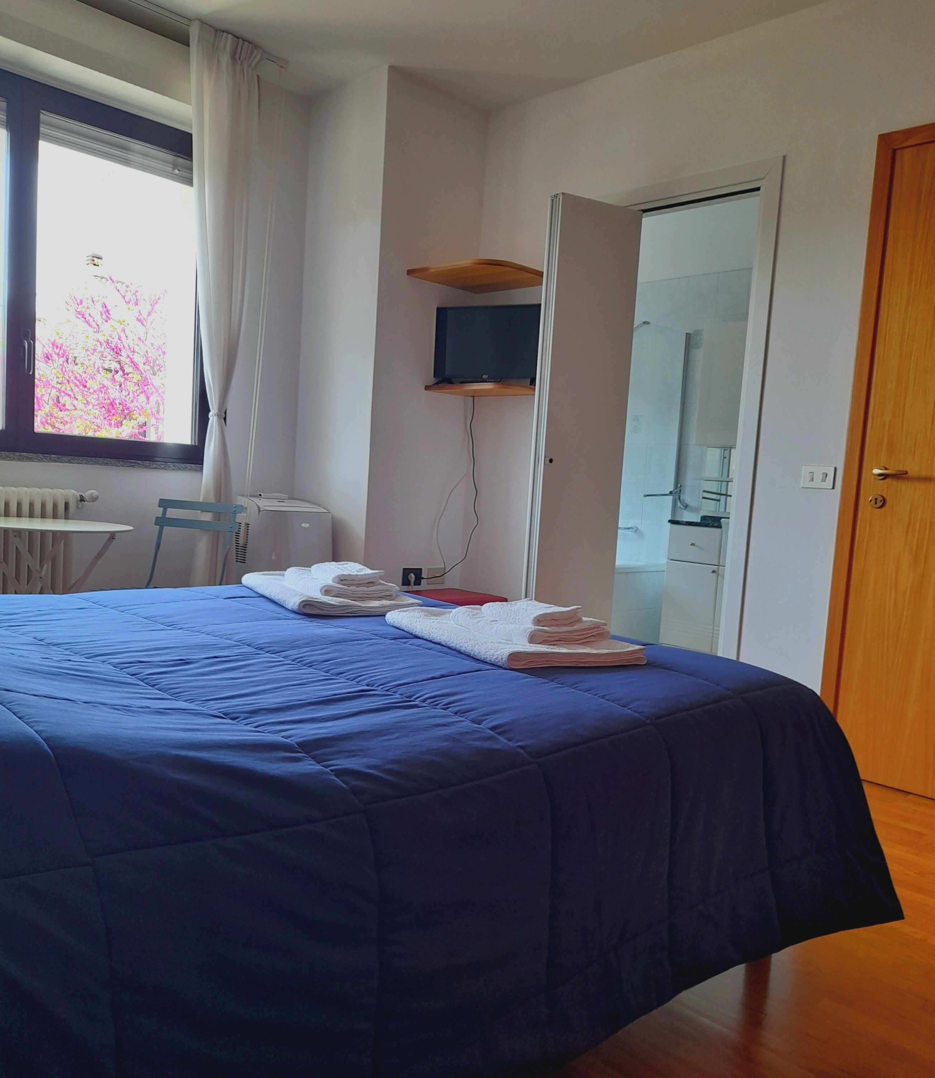 Un dormitorio con cama, una silla, televisor montado en la pared y una puerta.