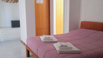 Un dormitorio con cama, puerta de madera, pared blanca y ventana.
