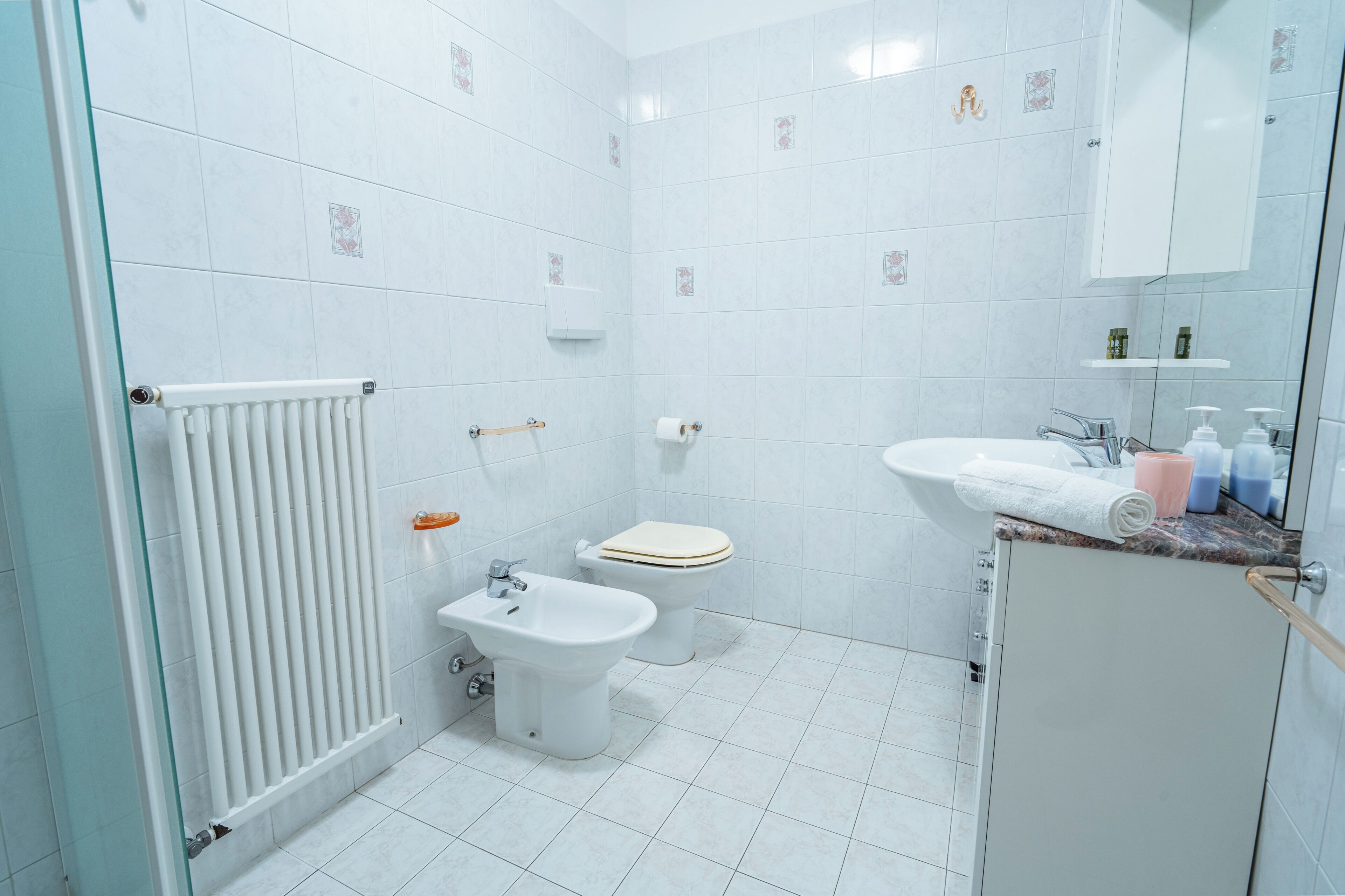 A bathroom with a toilet, bidet, sink, and radiator.