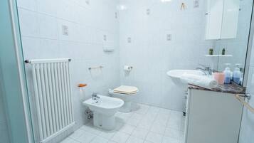 A bathroom with a toilet, bidet, sink, and radiator.