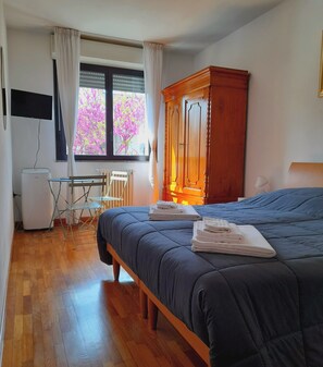Ein Schlafzimmer mit einem Bett, einem Holzschrank, einem Schreibtisch mit Stuhl, einer Heizung und einem Fenster mit Vorhängen.