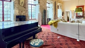 Ein Zimmer mit Klavier, Sofa, Lampe und einem gemusterten Teppich.