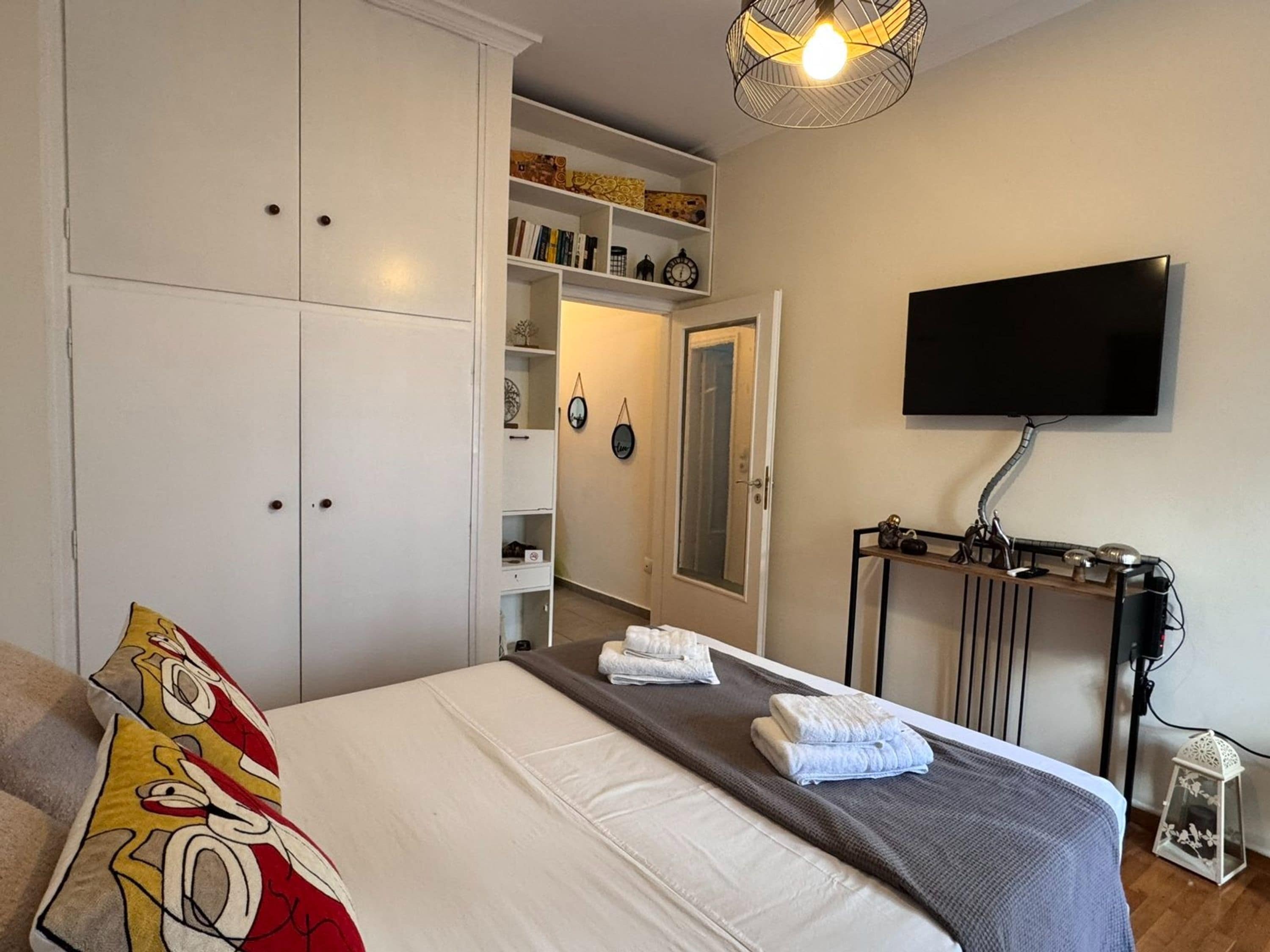 A bedroom with a bed, a wardrobe, a television, and a shelf with decorative items.