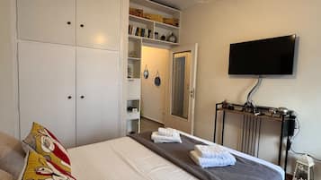 A bedroom with a bed, a wardrobe, a television, and a shelf with decorative items.