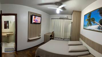Quarto com cama, televisão, aparelho de ar condicionado e pintura de uma praia.