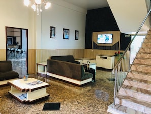 Un hall de hotel con asientos, un televisor y una escalera.