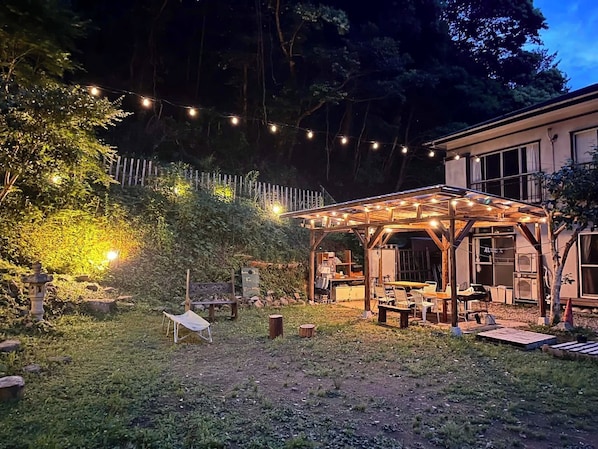 A covered outdoor area with string lights, a wooden pergola, and a small seating area with tables and chairs.
