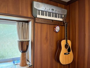 Una habitación con paredes de madera, una ventana con cortinas, un teclado, una batería y una guitarra acústica.