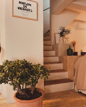 Eine Treppe führt zu einer Zwischenebene, wo ein Rahmen mit der Aufschrift 'MAISON DE VACANCES' und ein Blumentopf zu sehen sind.