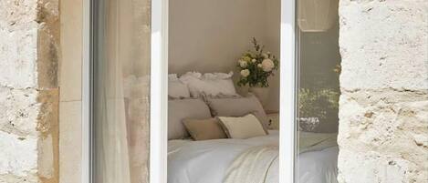 Een slaapkamer met een bed, een nachtkastje, een vaas met bloemen en een raam met gordijnen.