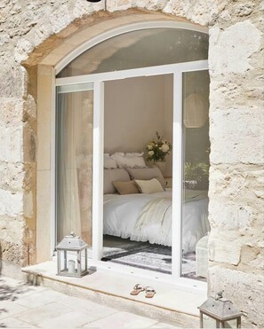 Ein Schlafzimmer mit Bett, Nachttisch, einer Blumenvase und einem Fenster mit Vorhängen.