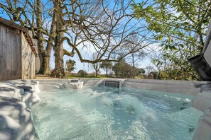 Een hottub met een houten terras en een ladder, omringd door bomen en een heldere lucht.