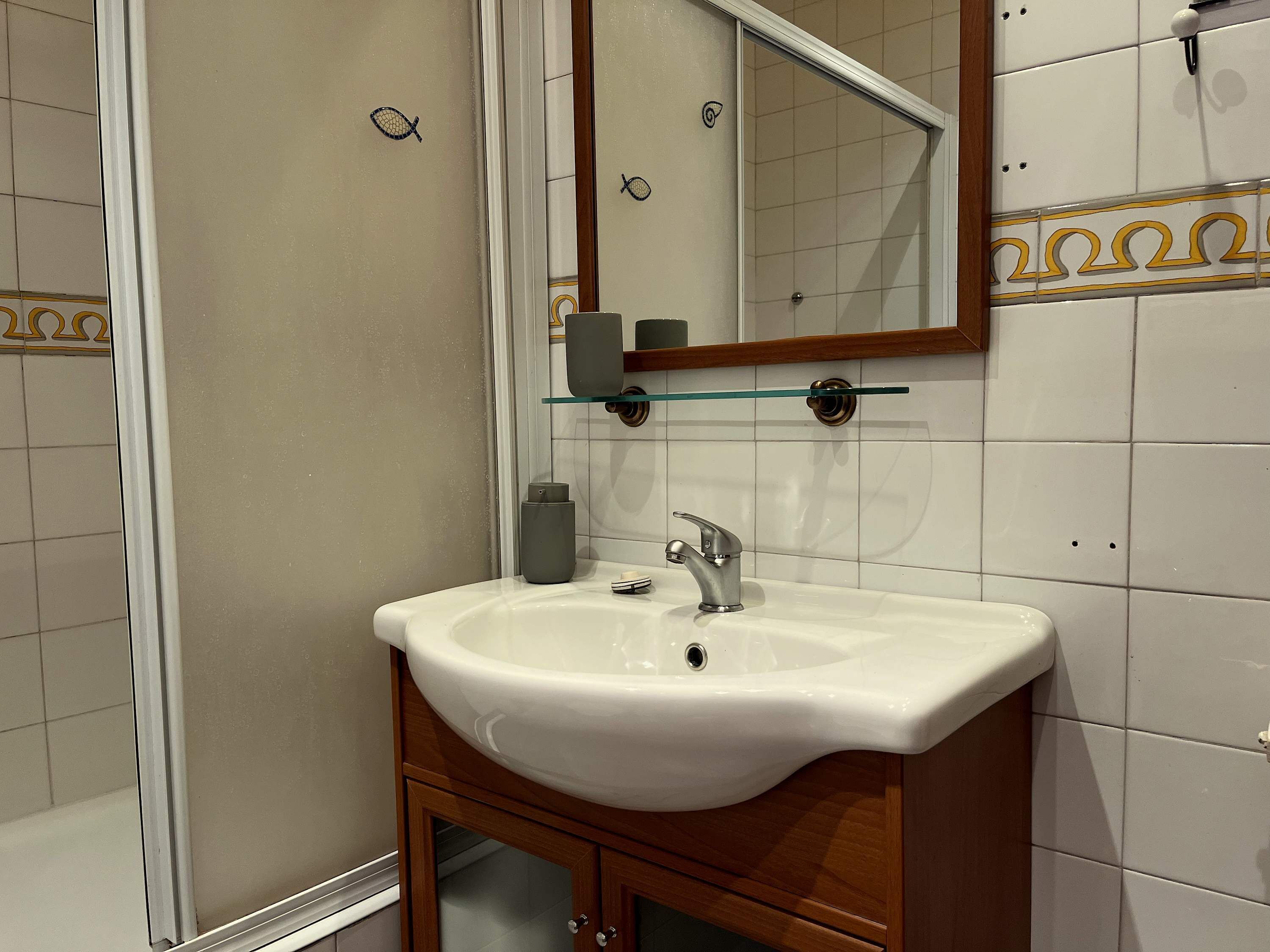 A bathroom with a white sink, a mirror, and a glass shelf.