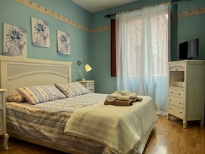 Un dormitorio con cama, mesita de noche, lámpara, cómoda y una obra de arte en la pared.