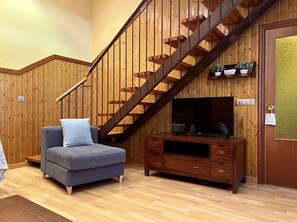 Een kamer met een houten trap, een bank, een tv-meubel en een deur met een geëtst glasraam.