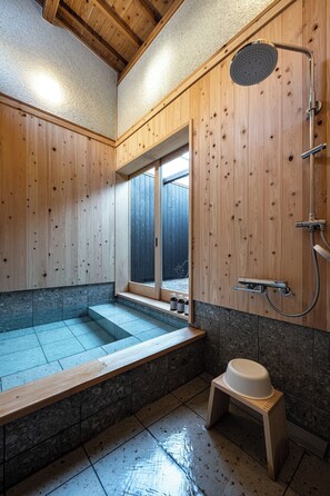 Une salle de spa en bois équipée d’un bain à remous, d’une douche et d’un petit tabouret.