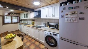 Une cuisine avec des meubles blancs, un lave-linge, un four à micro-ondes et un calendrier sur le réfrigérateur.