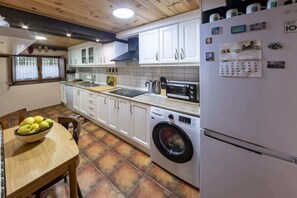 Eine Küche mit weißen Schränken, einer Waschmaschine, einer Mikrowelle und einem Kalender am Kühlschrank.