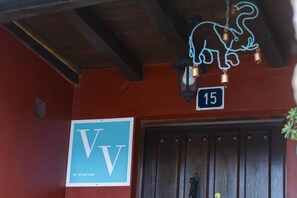 Ein Hotel Eingang mit einer Holztür, einem Neon-Wiesellogo und einem Schild mit den Buchstaben 'VV' und der Nummer '15'.