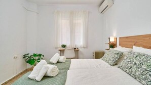 Et soveværelse med seng, puder, et natbord, en lampe, en radiator og et vindue med gardiner.