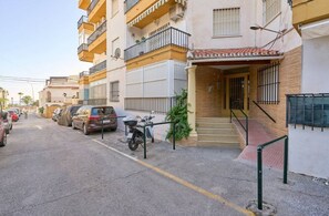 Une vue de rue montrant un immeuble avec une entrée carrelée, un escalier et un scooter garé.
