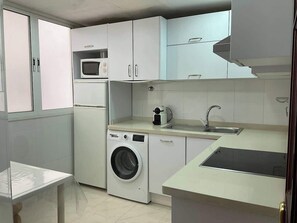 Cocina compacta con lavadora, microondas, pileta y una mesada pequeña.