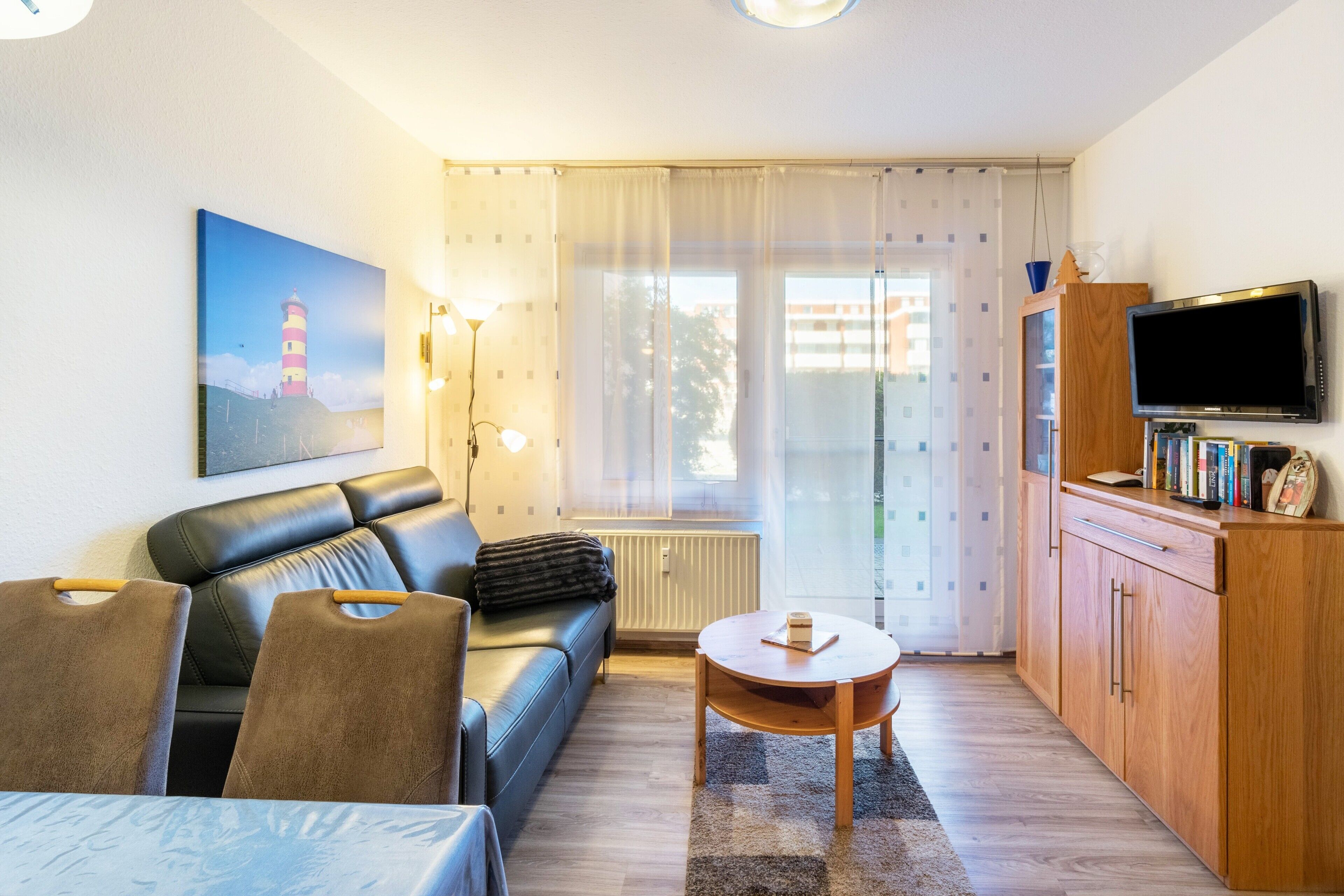 Een woonkamer met een bank, een tafel, een televisie en een schilderij van een vuurtoren.