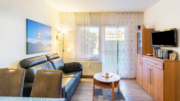 Een woonkamer met een bank, een tafel, een televisie en een schilderij van een vuurtoren.