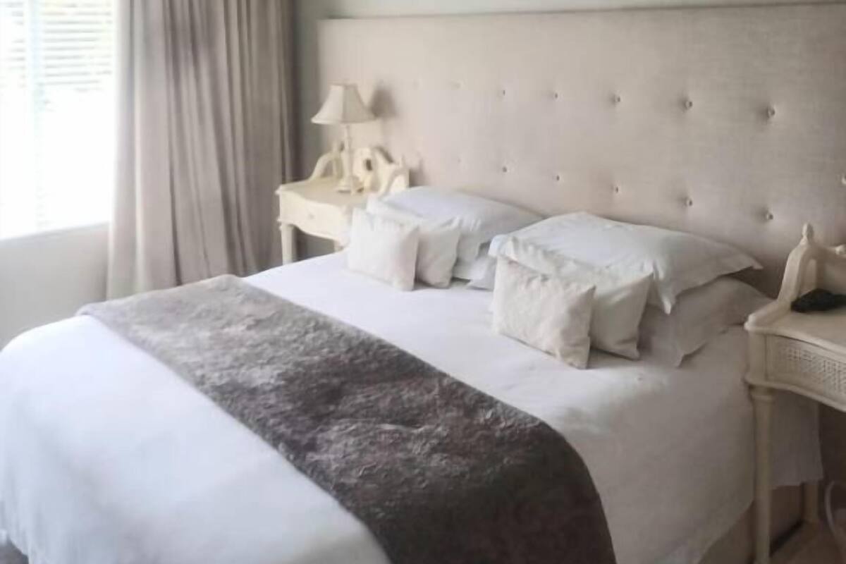 Una habitación de hotel con cama, mesita de noche, lámpara, unidad de aire acondicionado y ventana con cortinas.