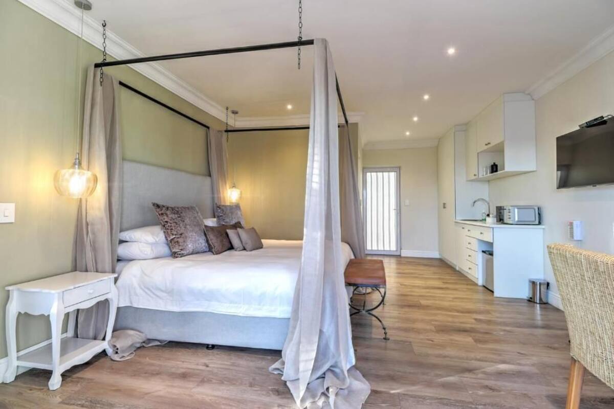 Un dormitorio con cama con dosel, mesita de noche, silla y un área de kitchenette.