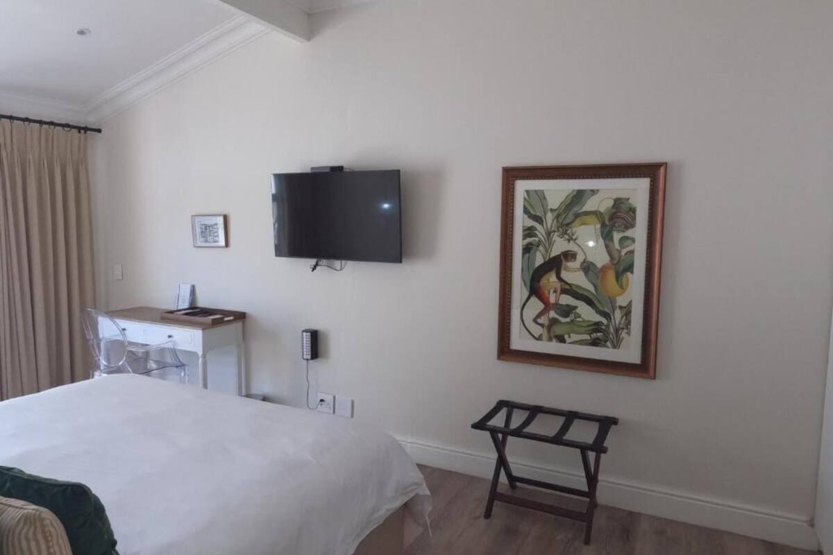 Una habitación de hotel con una cama, un escritorio con silla, un televisor montado en la pared y un cuadro enmarcado.