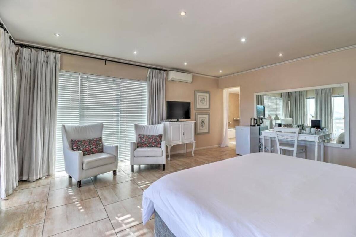 Habitación de hotel con una cama grande, un escritorio, una silla, un televisor y un espejo.