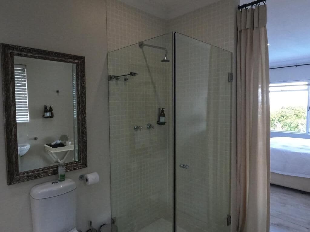 A bathroom with a glass-enclosed shower, a toilet, a sink, and a mirror.