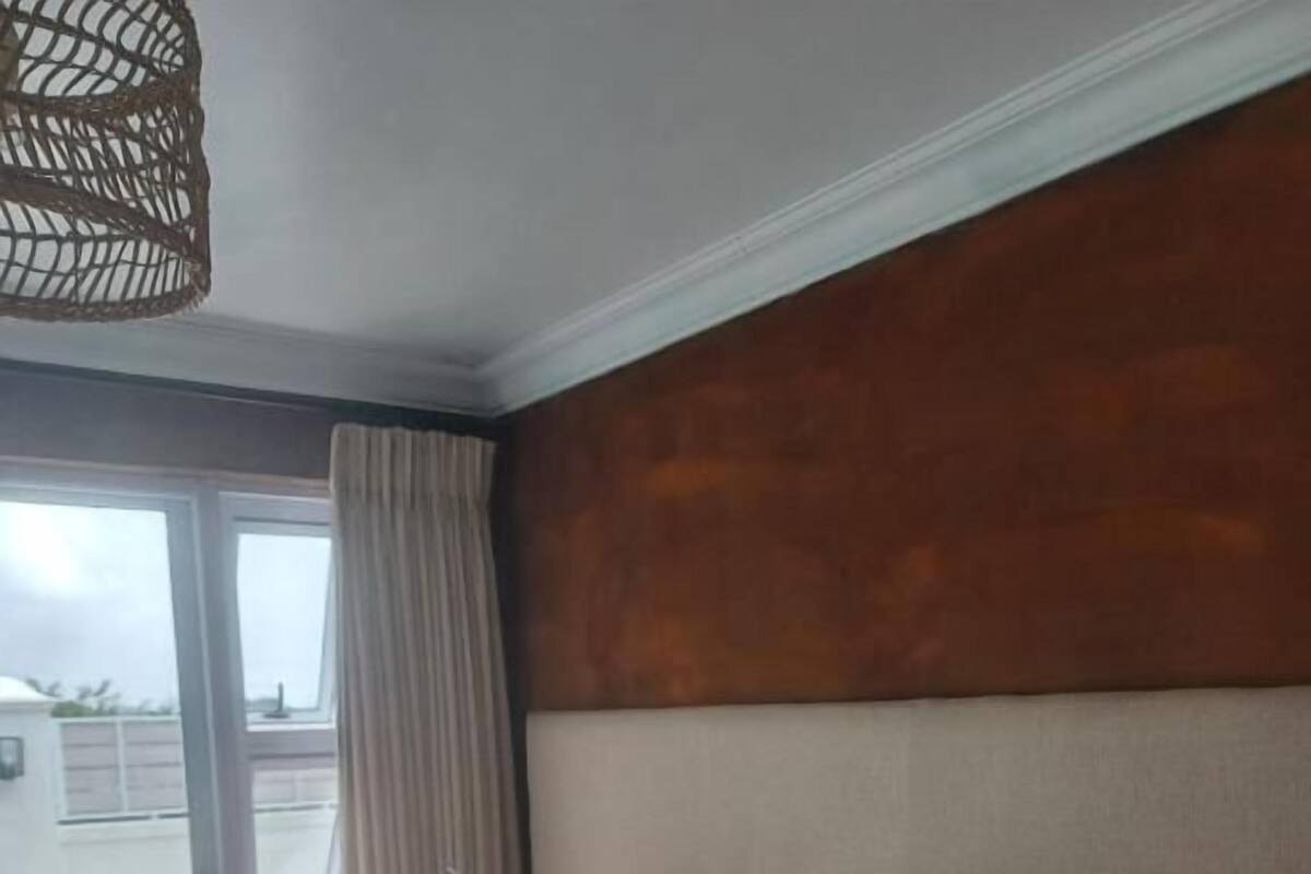 Habitación de hotel con cama, mesita de noche, lámpara y vistas a través de un ventanal.