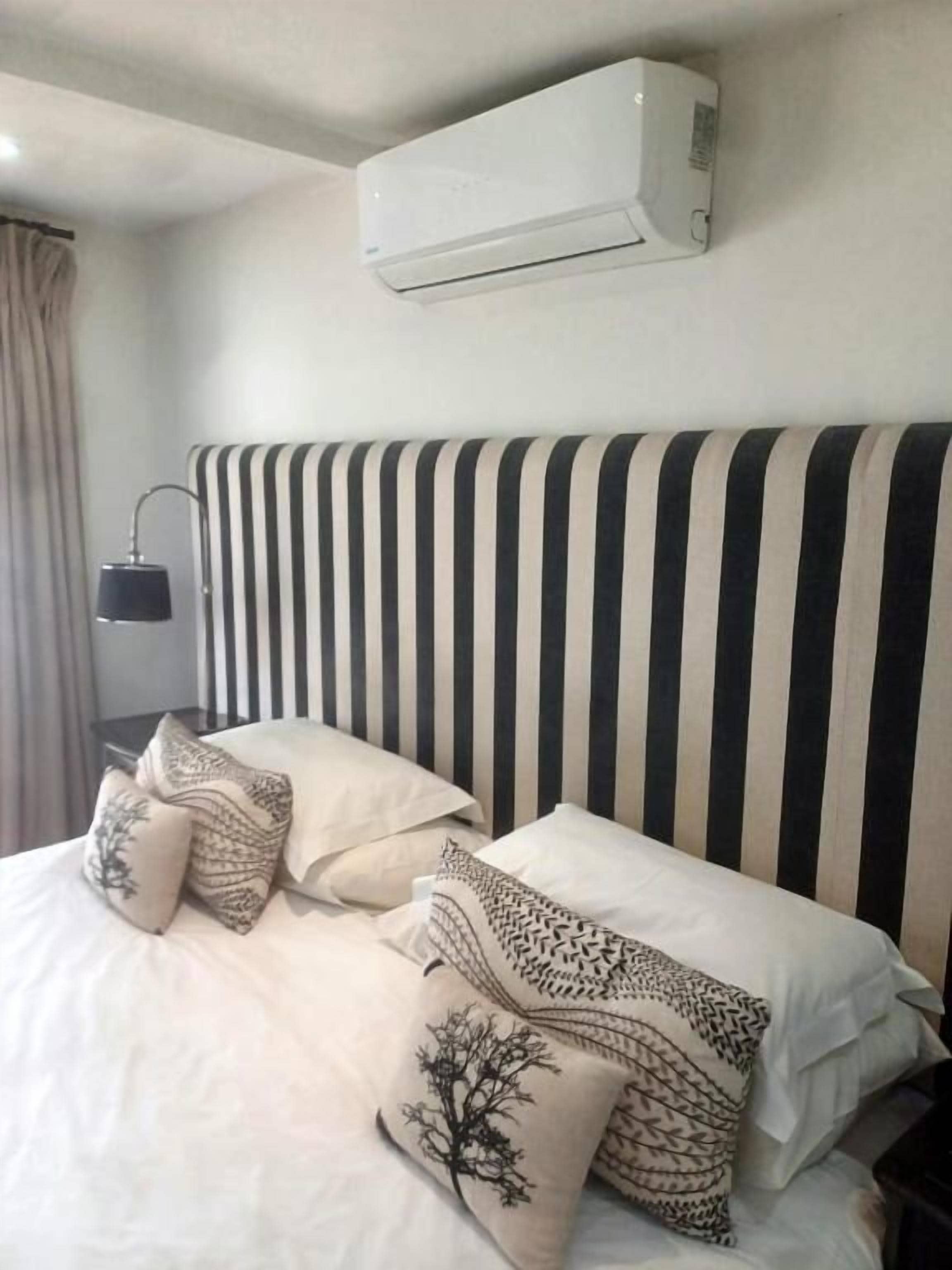 A bed with striped headboard, patterned pillows, and an air conditioning unit above.