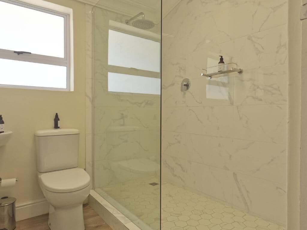 Un baño con inodoro, ducha con puerta de cristal y pared de mármol.