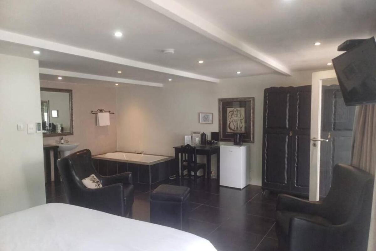 Una habitación de hotel con cama, escritorio, silla, kitchenette pequeña y televisor.