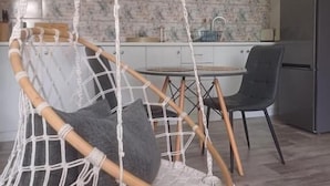 Una cocina moderna con armarios blancos, un sillón colgante de macramé y una mesa de comedor.