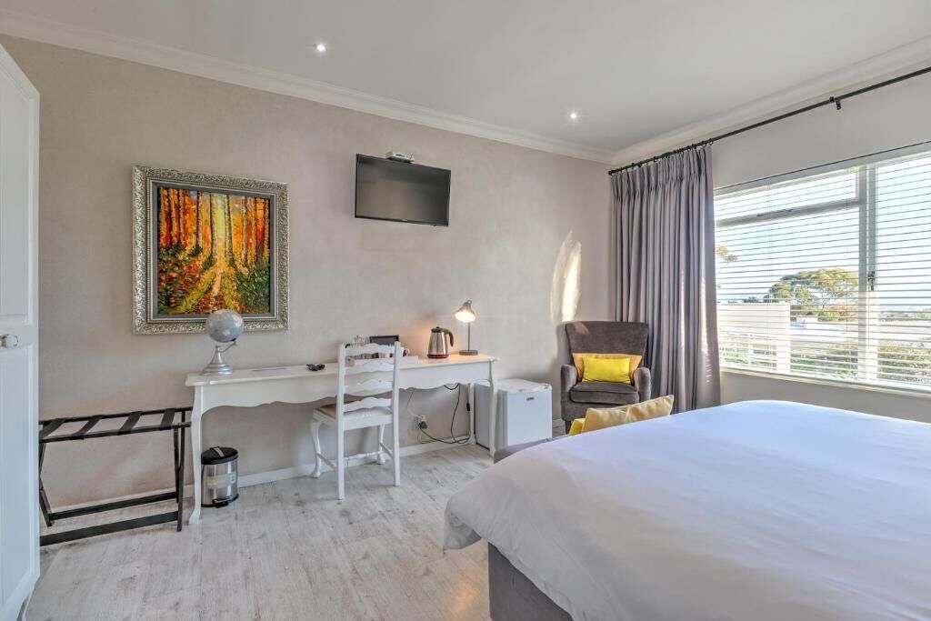 A hotel room with a bed, desk, chair, and a painting on the wall.