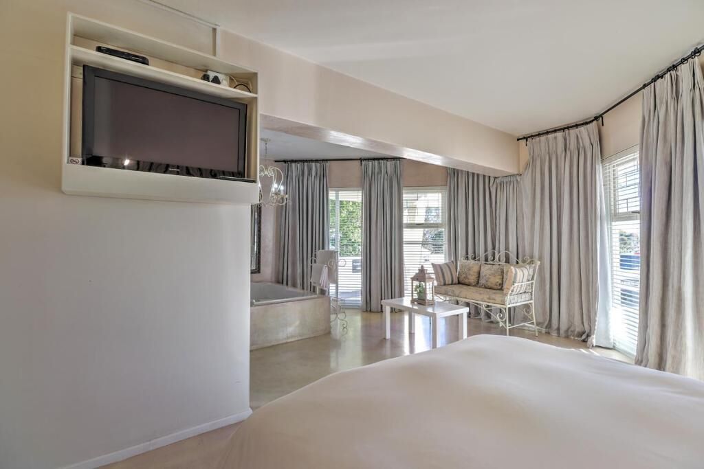 Ein Hotelzimmer mit Bett, Wand-Fernseher, einer Sitzecke mit Sofa und Sesseln sowie großen Fenstern mit Vorhängen.