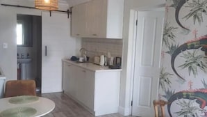 Una cocina moderna con armarios blancos, un comedor con una mesa y sillas redondas, y una sala de estar con sofá y reposapiés.