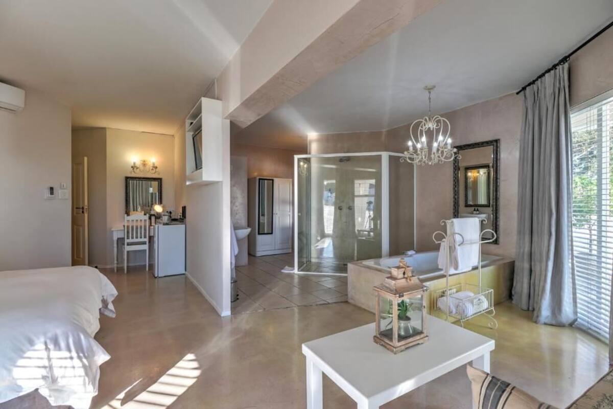 Habitación de hotel con cama, escritorio, ducha, tocador con espejo y ventana con cortinas.
