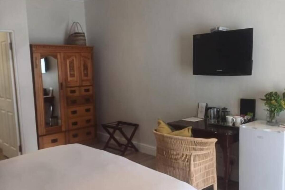 Un dormitorio con cama, un armario de madera, televisor, escritorio y un refrigerador pequeño.