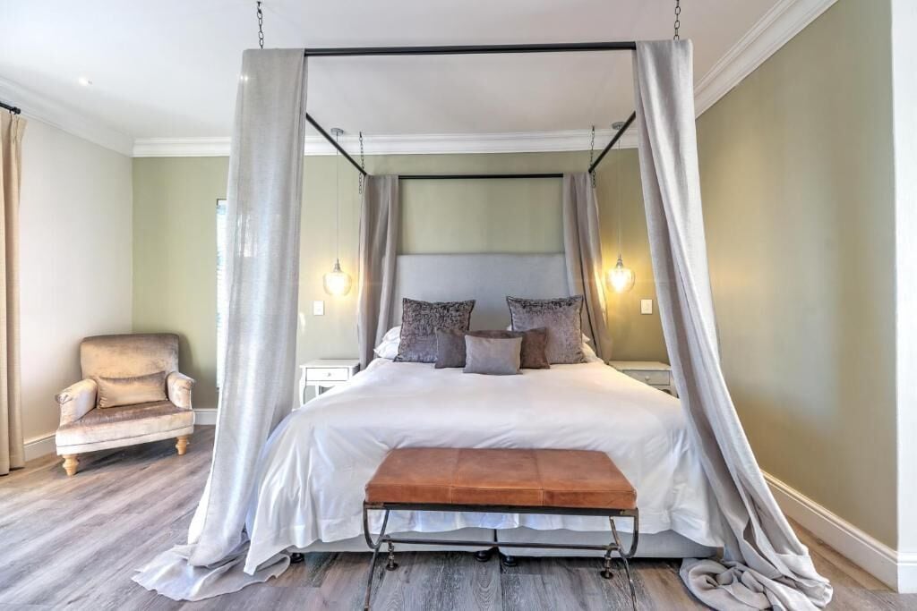 A four-poster canopy bed with a bench, a chair, and bedside lamps.