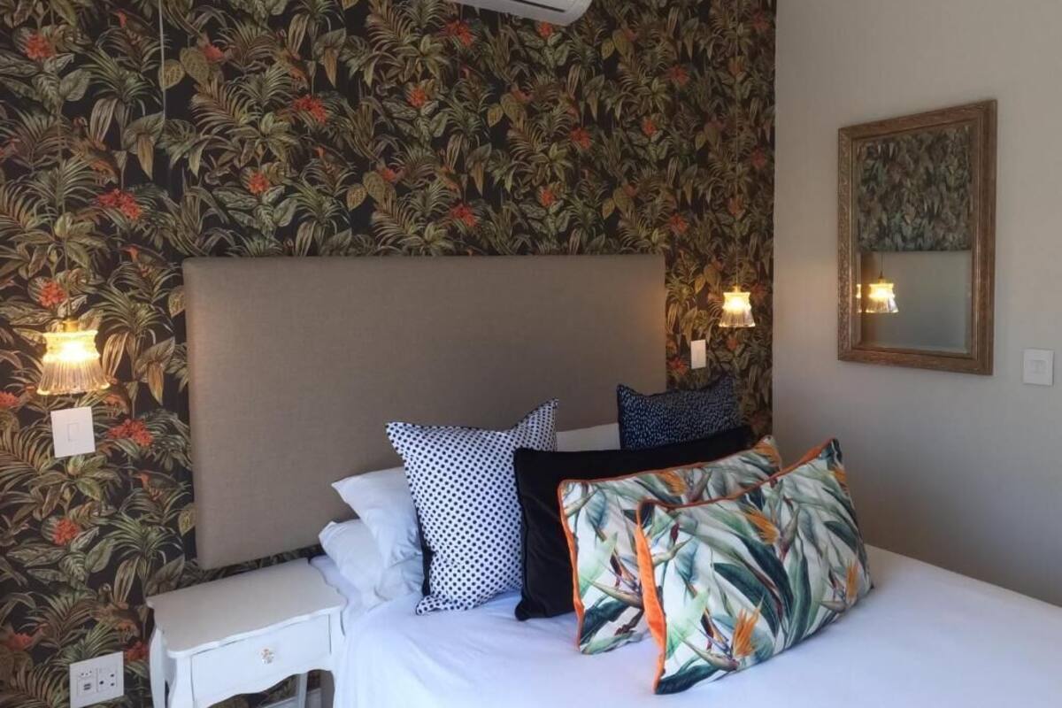 Una habitación de hotel con cama, mesita de noche, aire acondicionado instalado en la pared y un espejo.