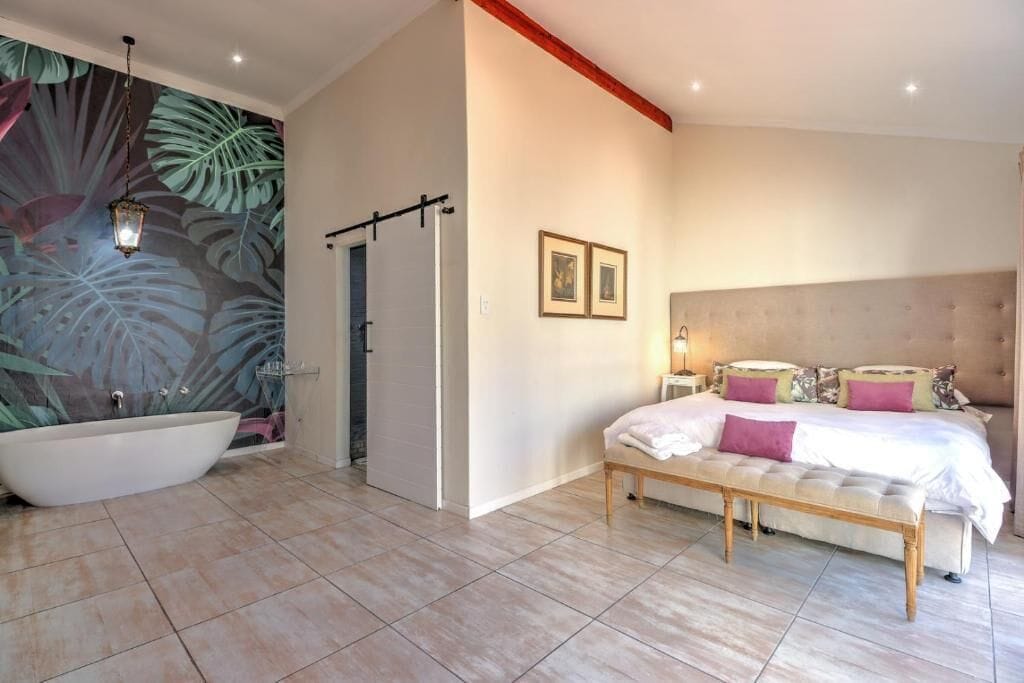 A bedroom with a large bathtub, a bed with multiple pillows, and a wall with framed pictures.