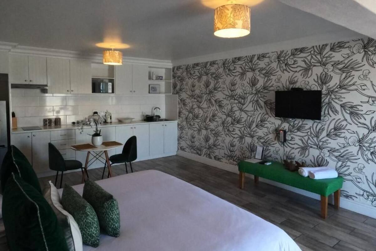 Una habitación de hotel moderna con una cama, un banco verde, una zona de comedor y una cocina.