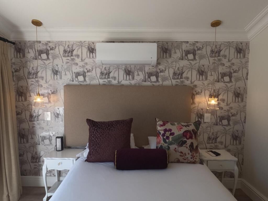 A bedroom with a large bed, two bedside tables, a wall-mounted air conditioner, and patterned wallpaper.